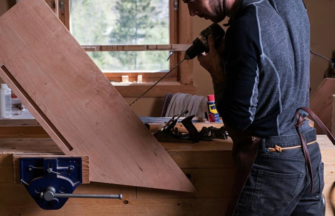 Zdenko drilling into a board at the workbench in the workshop in Tessungdalen